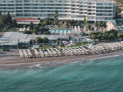 Großes Hotel mit Pool, Sonnenschirmen und Liegestühlen am Strand neben klarem Meer.