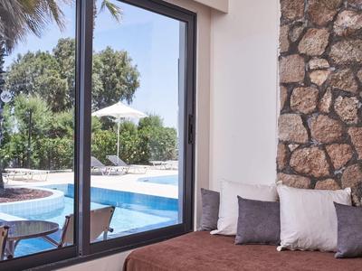 Moderne Hotelterrasse mit Pool, Glasfenstern, Palmen und bequemen Sitzkissen an der Wand.