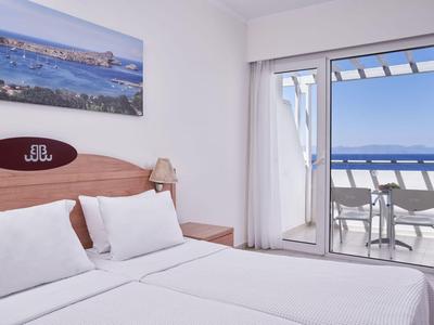 Helles Hotelzimmer mit Doppelbett und Balkon mit Meerblick.