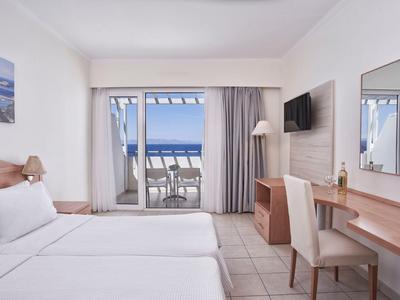Hotelzimmer mit zwei Betten, Schreibtisch, Fernseher und Balkon mit Meerblick.