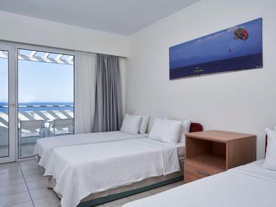 Helle Hotelzimmer mit zwei weißen Betten und Balkon mit Meerblick.