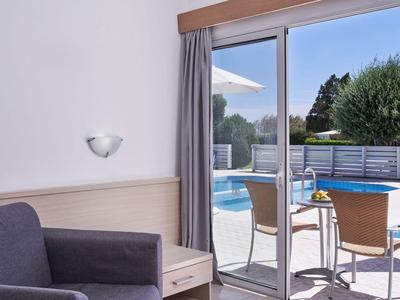 Moderner Hotelraum mit Glas-Schiebetür zum Balkon und Poolblick bei sonnigem Wetter.