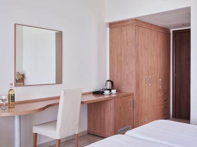 Hotelzimmer mit Holzmöbeln, Spiegel, bequemen Stuhl und Doppelbett in hellem Raum.