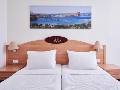 Ein Doppelbett mit weißen Bettwaren und Nachttischen in einem Hotelzimmer mit Meeresbild an der Wand.
