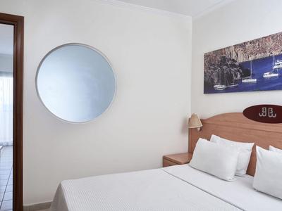 Schlicht eingerichtetes Hotelzimmer mit Doppelbett, rundem Spiegel und maritimem Wandbild.