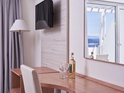 Hotelzimmer mit Schreibtisch, Stuhl, Flasche und Glas, Blick auf Terrasse mit Meer.