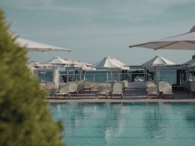 Moderner Hotelpool mit Sonnenliegen und weißen Sonnenschirmen unter bewölktem Himmel.