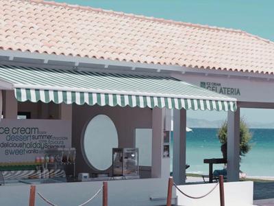 Strandrestaurant mit weiß-grün gestreiftem Sonnenschutz am Meer bei klarem Himmel.