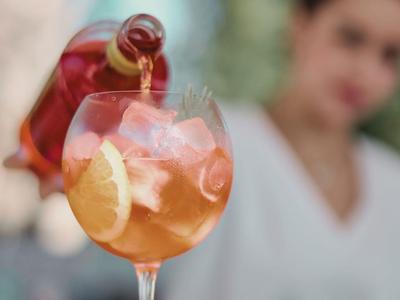 Ein Getränk mit Orangenscheibe und Eis wird in ein Glas eingeschenkt.