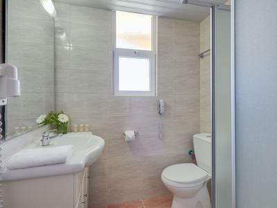 Bright hotel bathroom with white sink, toilet, mirror, and a small window.
