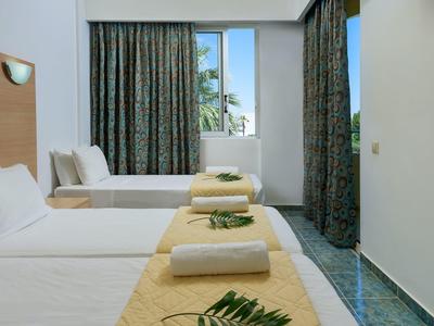Bright hotel room with two single beds, yellow bed runners, and a window with closed curtains.