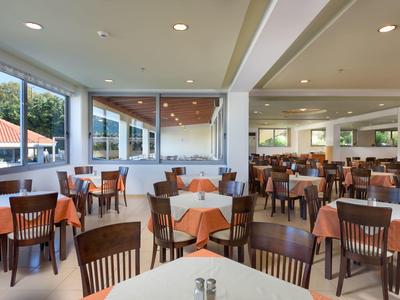 Spacious dining area with wooden chairs and tables covered with orange tablecloths, large windows.