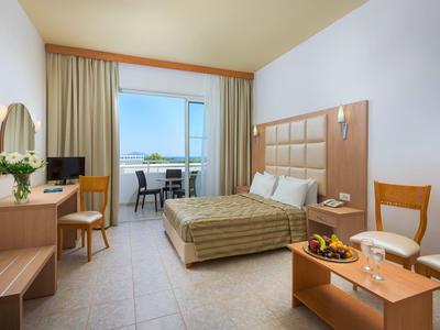 Hotel room with double bed, desk, chairs, balcony, and sea view through glass door.