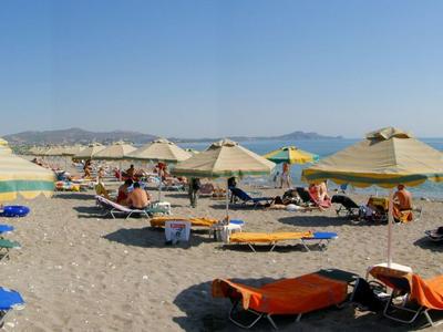 Sunny beach with umbrellas and lounge chairs by the clear blue sea under a bright sky.