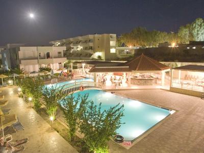Night view of a lit hotel pool area with sun loungers, umbrellas, and moonlit sky.