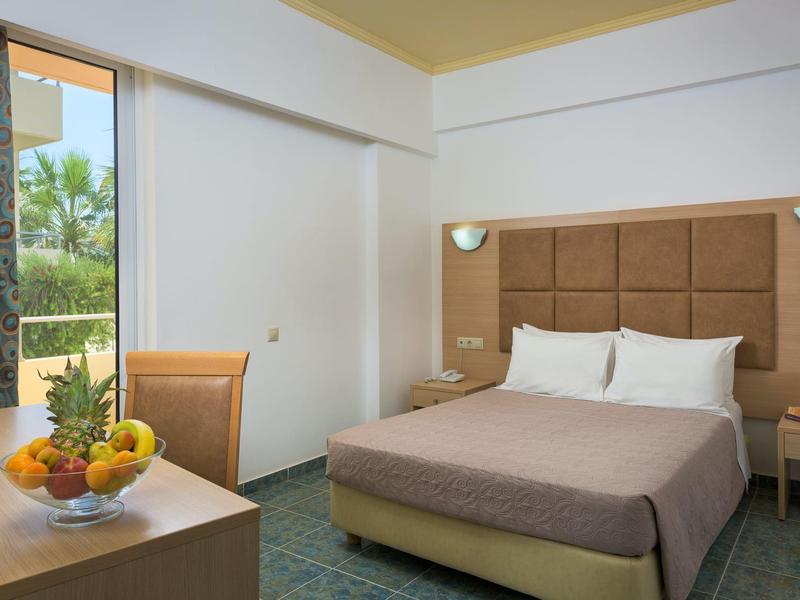 Hotel room with double bed, brown headboard, bedside tables, fruit bowl, and window with curtains.