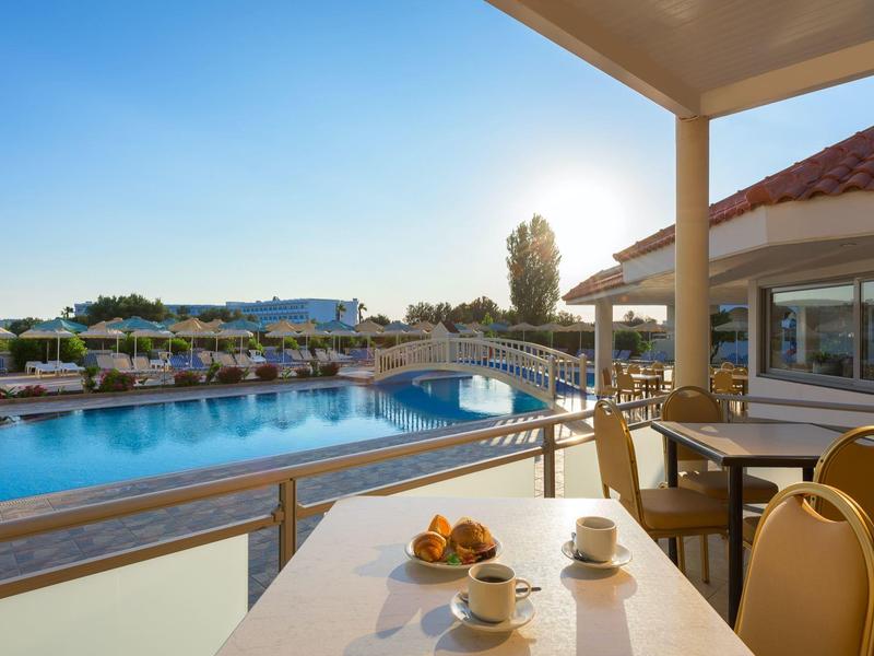 Hotel balcony with table, chairs, and view of a pool under clear blue sky at sunset.