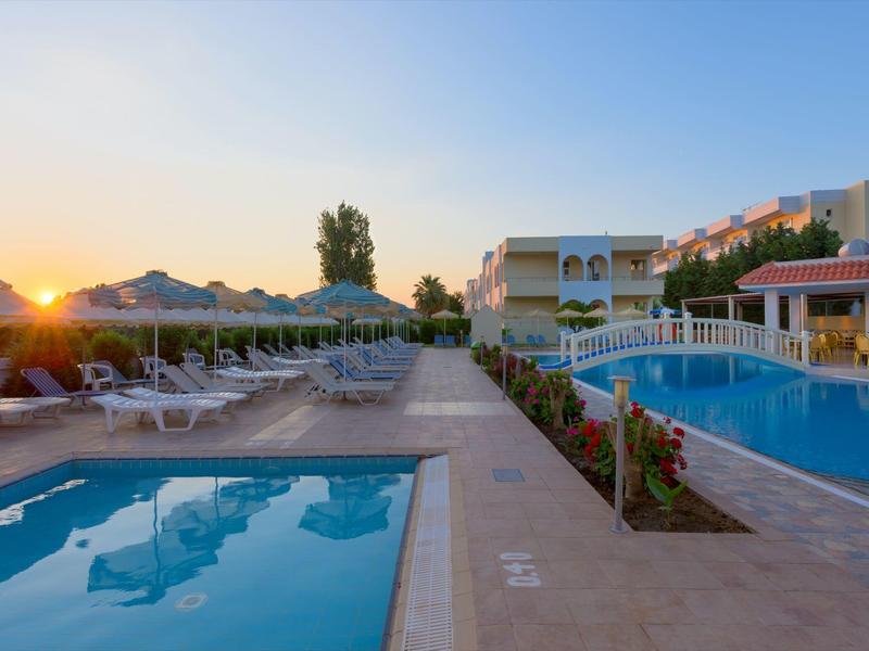 Outdoor pool area at sunset with lounge chairs, umbrellas, and surrounding buildings.