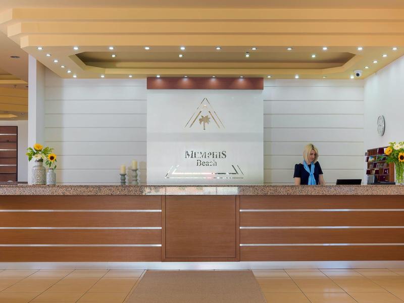 Modern hotel reception with wooden desk, a staff member, and decorative flowers.