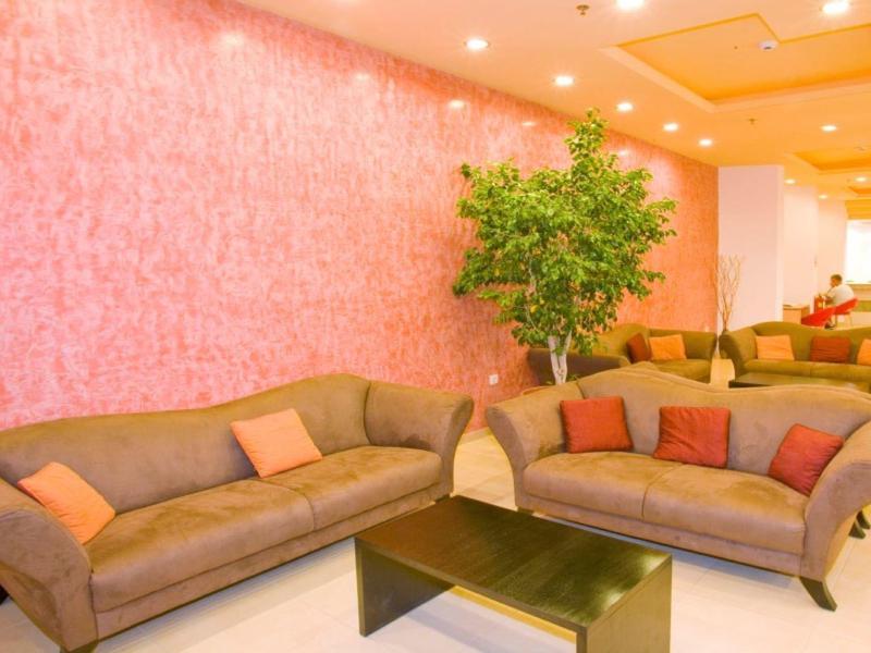 Bright hotel lounge with pink walls, brown sofas, cushions, green plant, and black table.