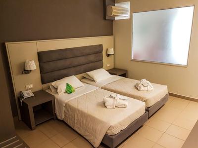 Pokój hotelowy z dwoma pojedynczymi łóżkami, stolikami nocnymi, lampami i mlecznym oknem.