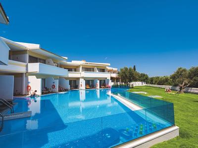 Ośrodek z dużym basenem infinity, białe budynki, zielony trawnik i czyste niebieskie niebo.