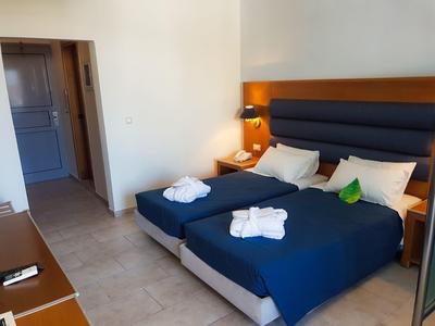 Pokój hotelowy z dwoma pojedynczymi łóżkami, niebieskimi narzutami, szlafrokami i lampkami nocnymi