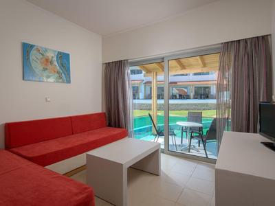 Pokój hotelowy z czerwoną sofą, białym stolikiem, telewizorem i balkonem z widokiem na basen.