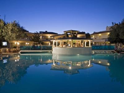 Luxushotel mit beleuchtetem Pool und Pavillon bei klarem Abendhimmel, umgeben von Bäumen.