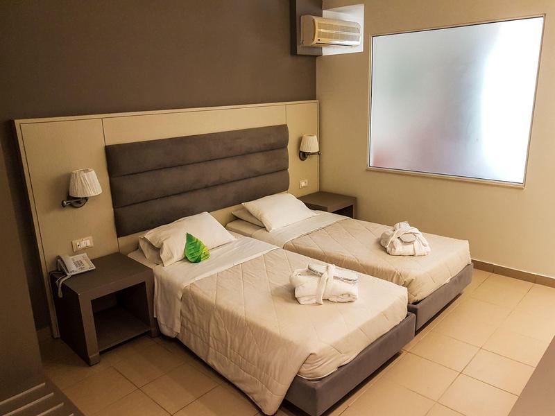 Pokój hotelowy z dwoma pojedynczymi łóżkami, stolikami nocnymi, lampami i mlecznym oknem.