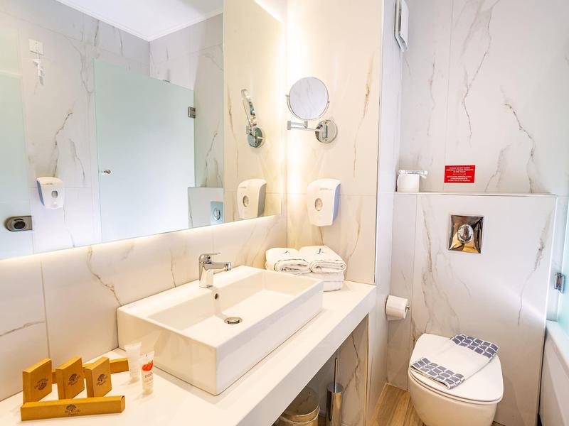 Jasna łazienka z dużym lustrem, białą umywalką i nowoczesną toaletą z marmurowymi ścianami.