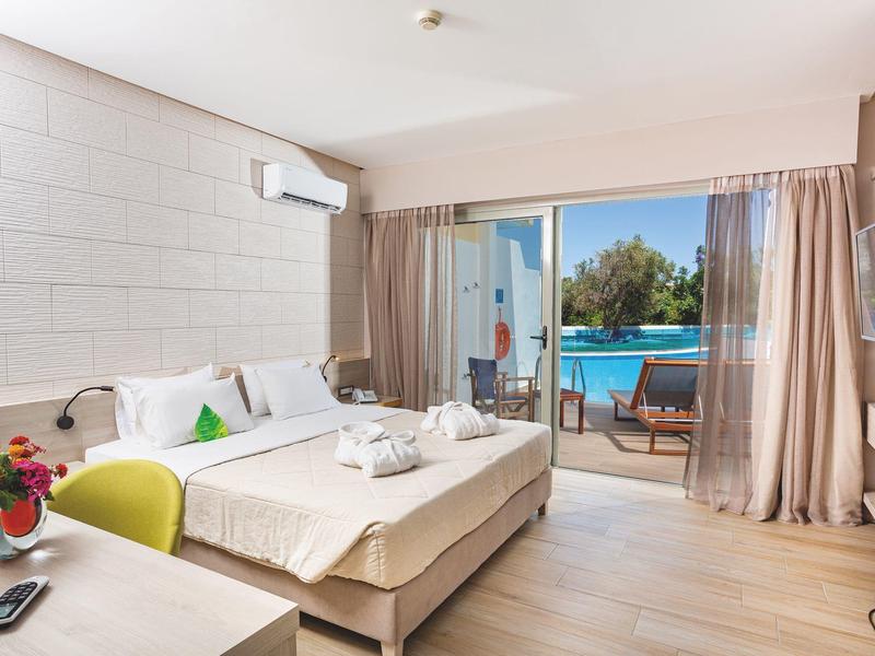 Jasny pokój hotelowy z podwójnym łóżkiem, biurkiem i przesuwanymi drzwiami na patio z widokiem na basen.