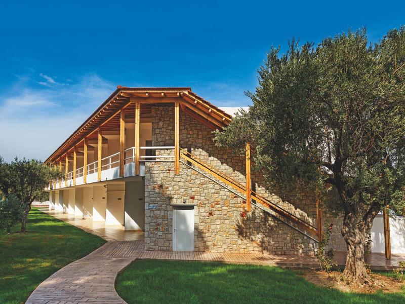 Dom z kamienia i drewna z balkonem otoczony zielonymi drzewami pod niebieskim niebem.