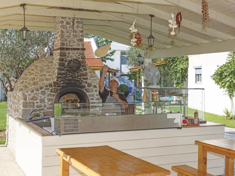 Zewnętrzne miejsce na grilla z kamiennym piecem, drewnianymi stołami i suszonymi papryczkami.