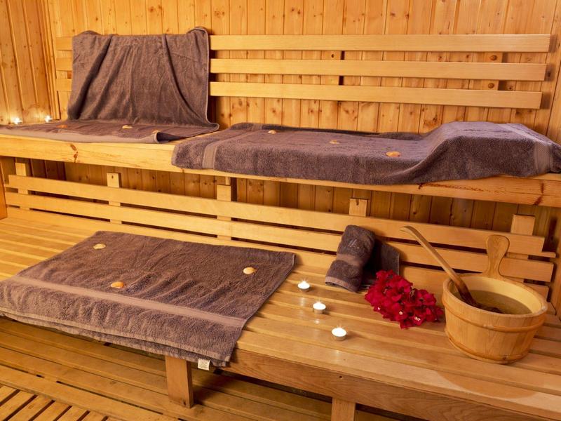 Przytulne drewniane wnętrze sauny z ręcznikami, świecami, płatkami róż i wiadrem do wody.