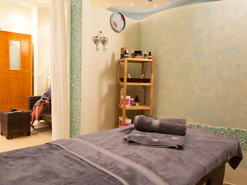 Przytulny pokój spa z stołem do masażu, szarymi ręcznikami, półką z olejkami i miękkim oświetleniem.