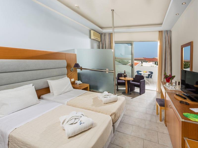 Jasny pokój hotelowy z dwoma łóżkami, balkonem i widokiem na morze.