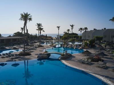 Vista de una gran piscina de hotel con tumbonas y palmeras bajo un cielo despejado.