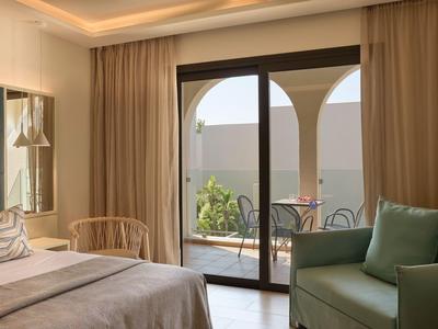 Habitación de hotel acogedora con cama, sillón y balcón con vista al jardín.