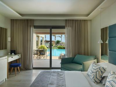 Habitación de hotel moderna con cama, área de estar y vista a la piscina a través de una gran puerta corredera de vidrio.