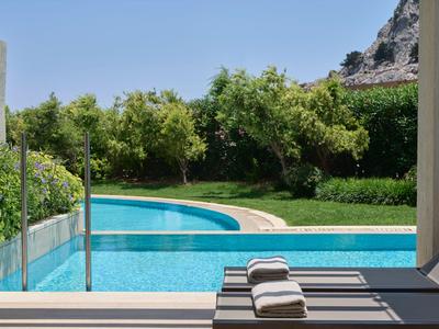 Piscina moderna con tumbonas y toallas frente a jardín verde y cielo azul