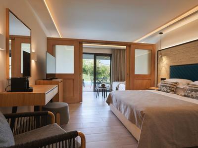 Habitación de hotel moderna con cama doble, escritorio y balcón con vistas a la vegetación.