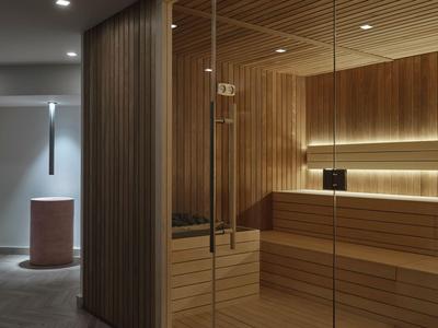 Sala de sauna moderna con paneles de madera y pared de vidrio, luz cálida resalta el interior.