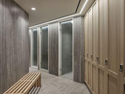 Vestuario moderno con taquillas de madera, banco e iluminación indirecta.