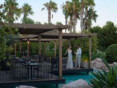Dos personas están en una terraza junto a un restaurante rodeado de palmeras.