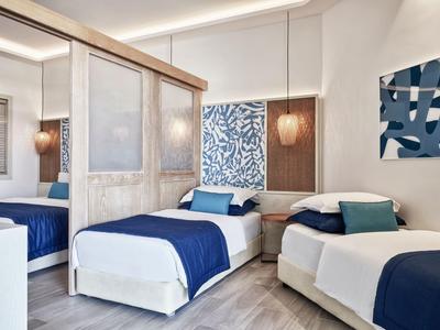 Habitación de hotel moderna con dos camas individuales, colchas azules y luz decorativa en la pared.