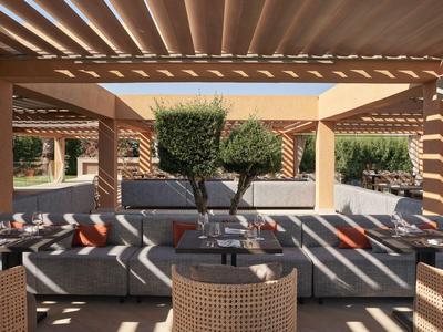 Terraza soleada con sofás y mesas bajo una pérgola de madera junto a un jardín cuidado.