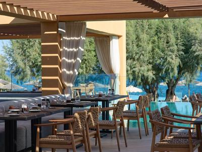 Área de restaurante abierta y cubierta con sillas de madera con vista al mar y árboles.