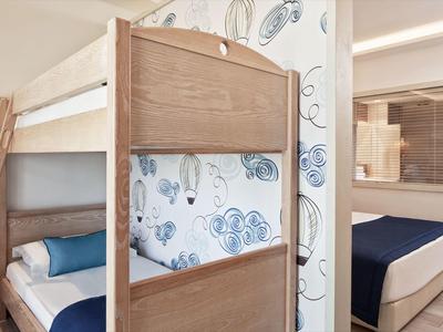 Kinderzimmer mit Holz-Etagenbett, blauer Bettwäsche und Tapete mit Blumenmuster, angrenzendes Schlafzimmer.