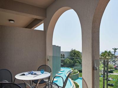 Balcón con arcos, mesa y sillas con vistas a la piscina, jardín y mar al fondo.